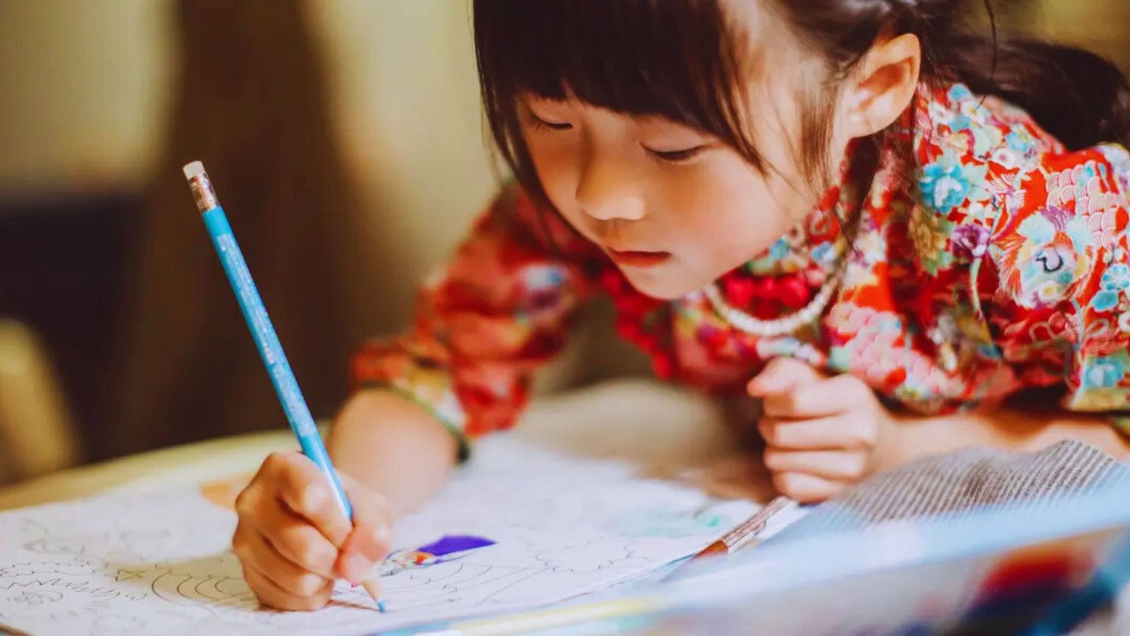 A young girl is focused on drawing on a piece of paper with colorful crayons.