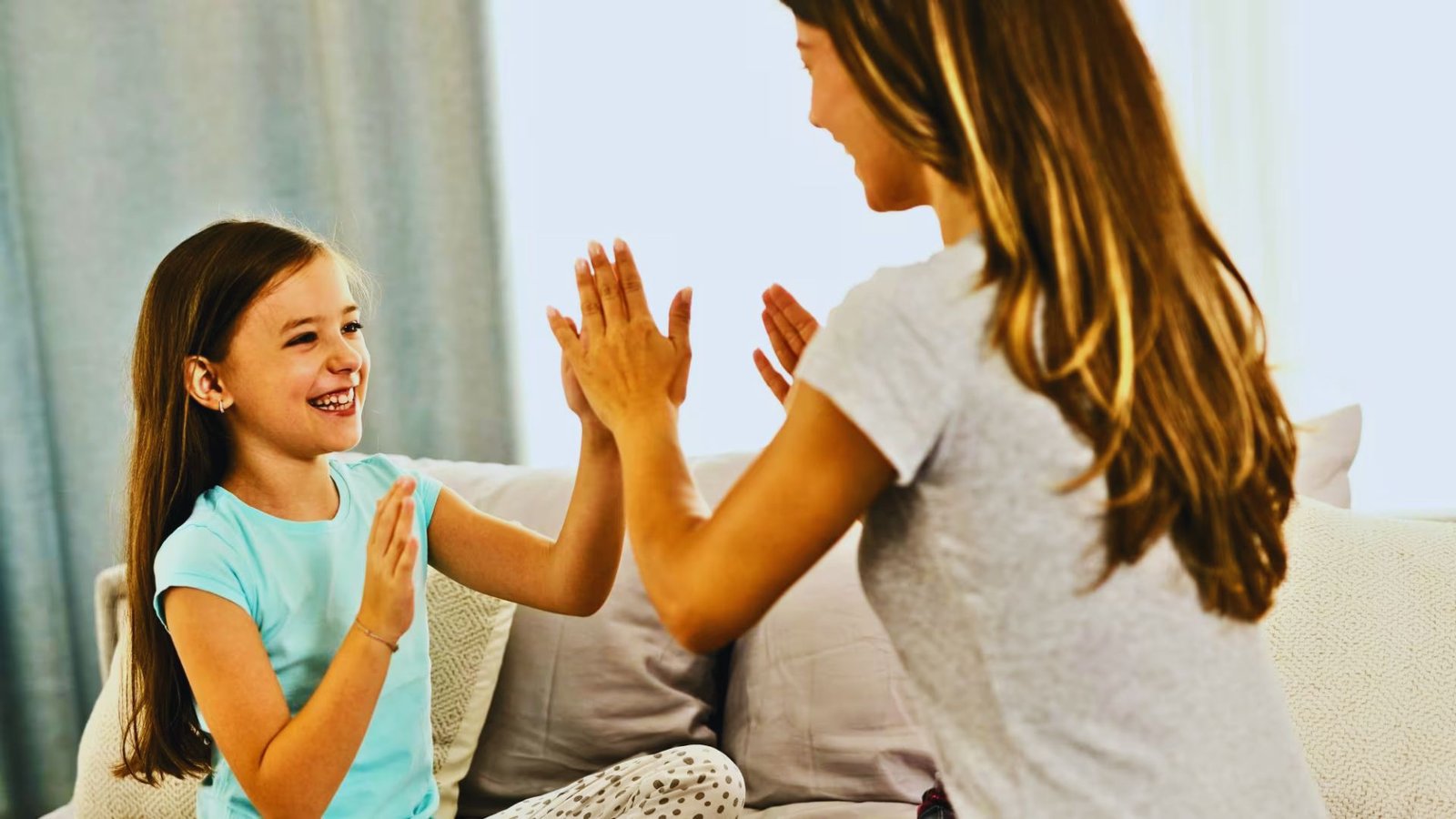 A woman and a young girl sit on a couch, joyfully giving each other high fives.