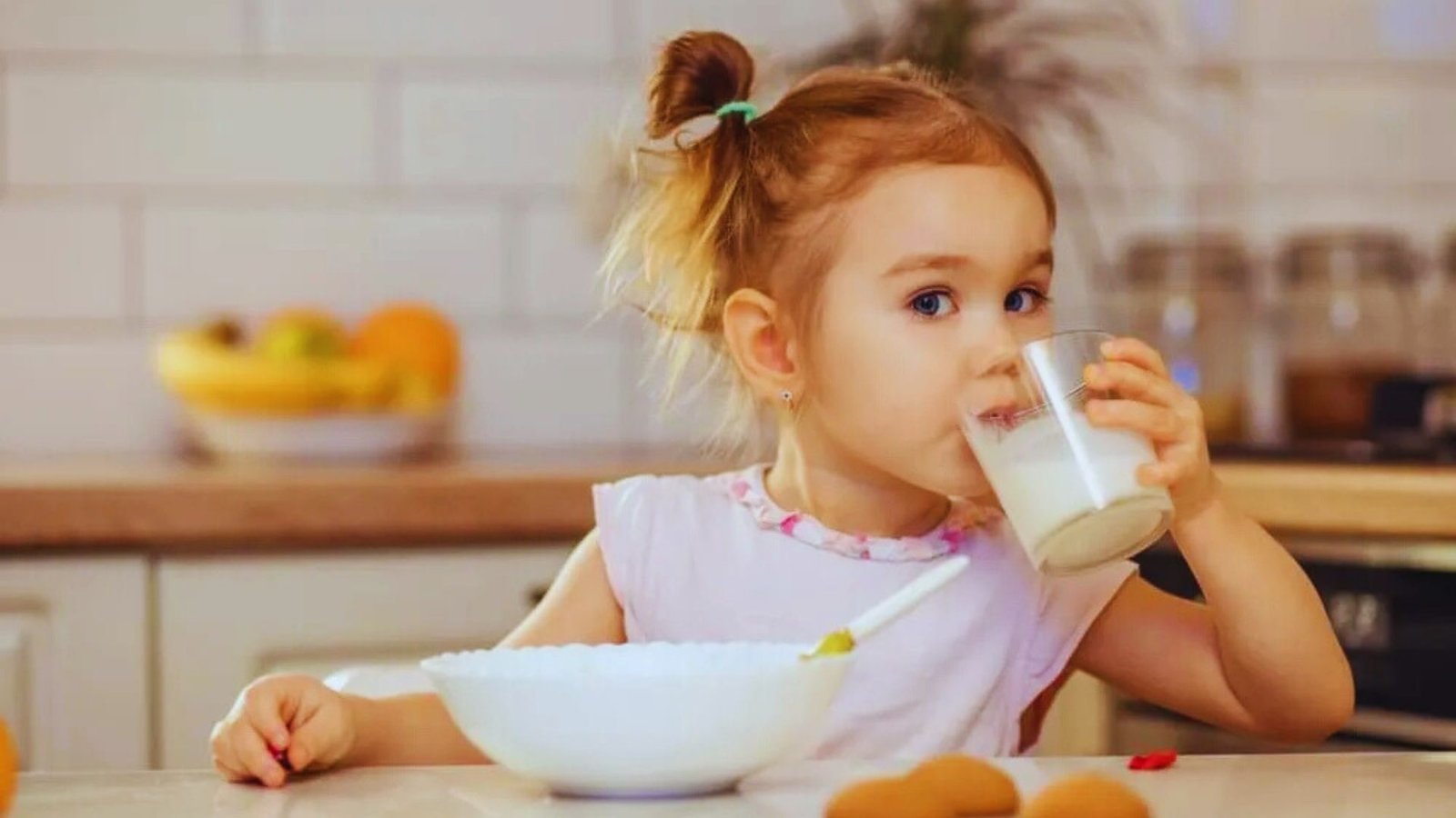 A little girl happily drinks milk from a glass, emphasizing the importance of protein for toddlers' growth and health.