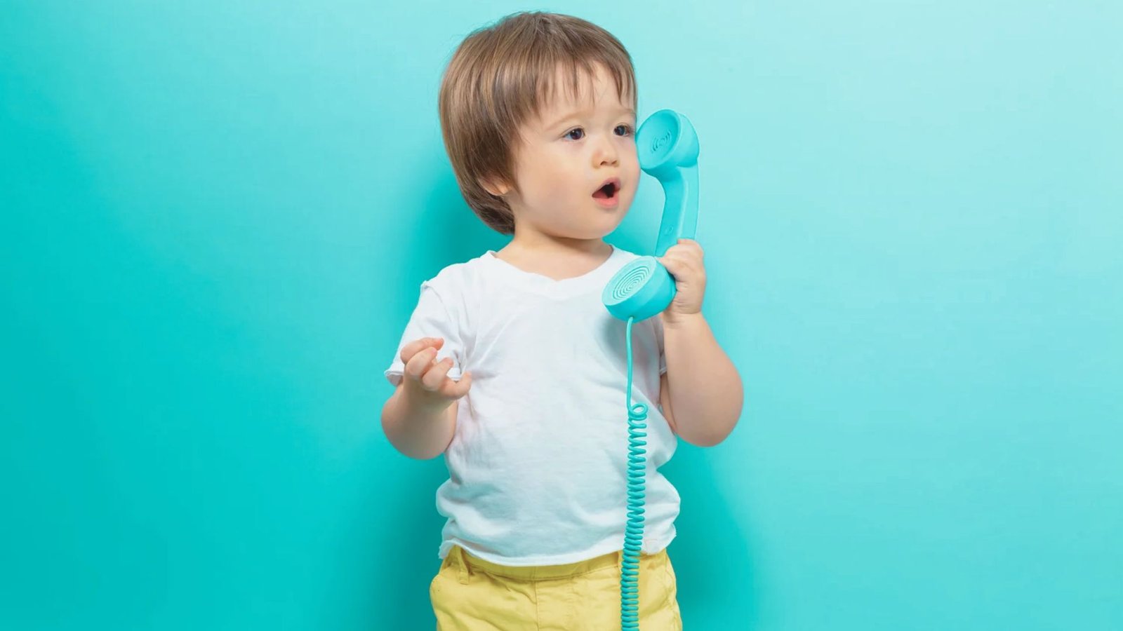 A young child holds a telephone against a blue background, smiling and looking engaged in conversation.