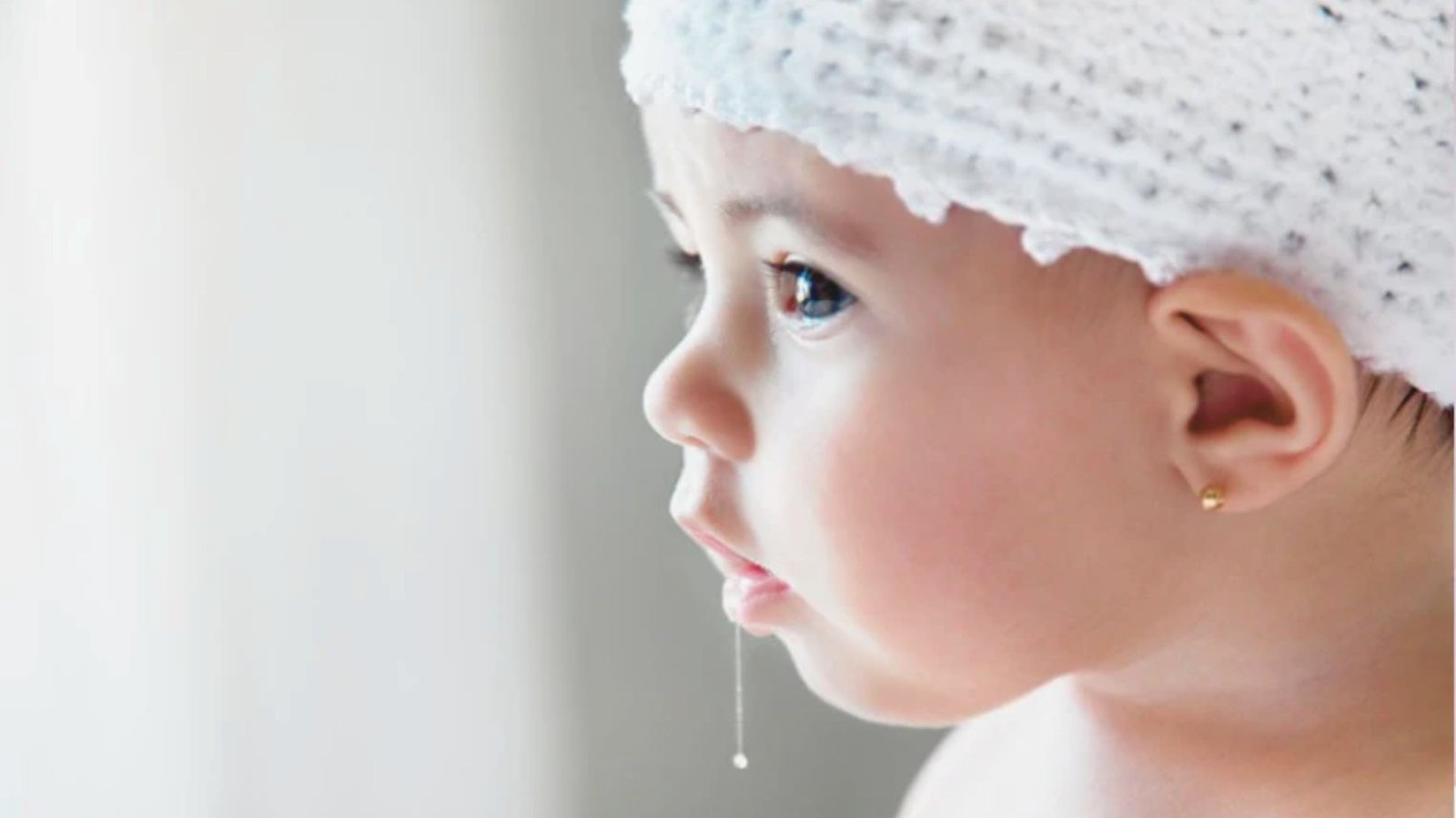 An infant dressed in a soft white knitted hat, exuding cuteness and warmth.
