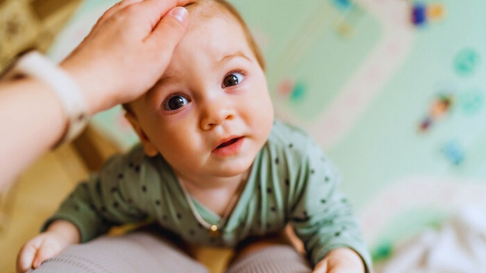 A baby gazes up at the camera while being cradled in the arms of an adult, showcasing a moment of connection.