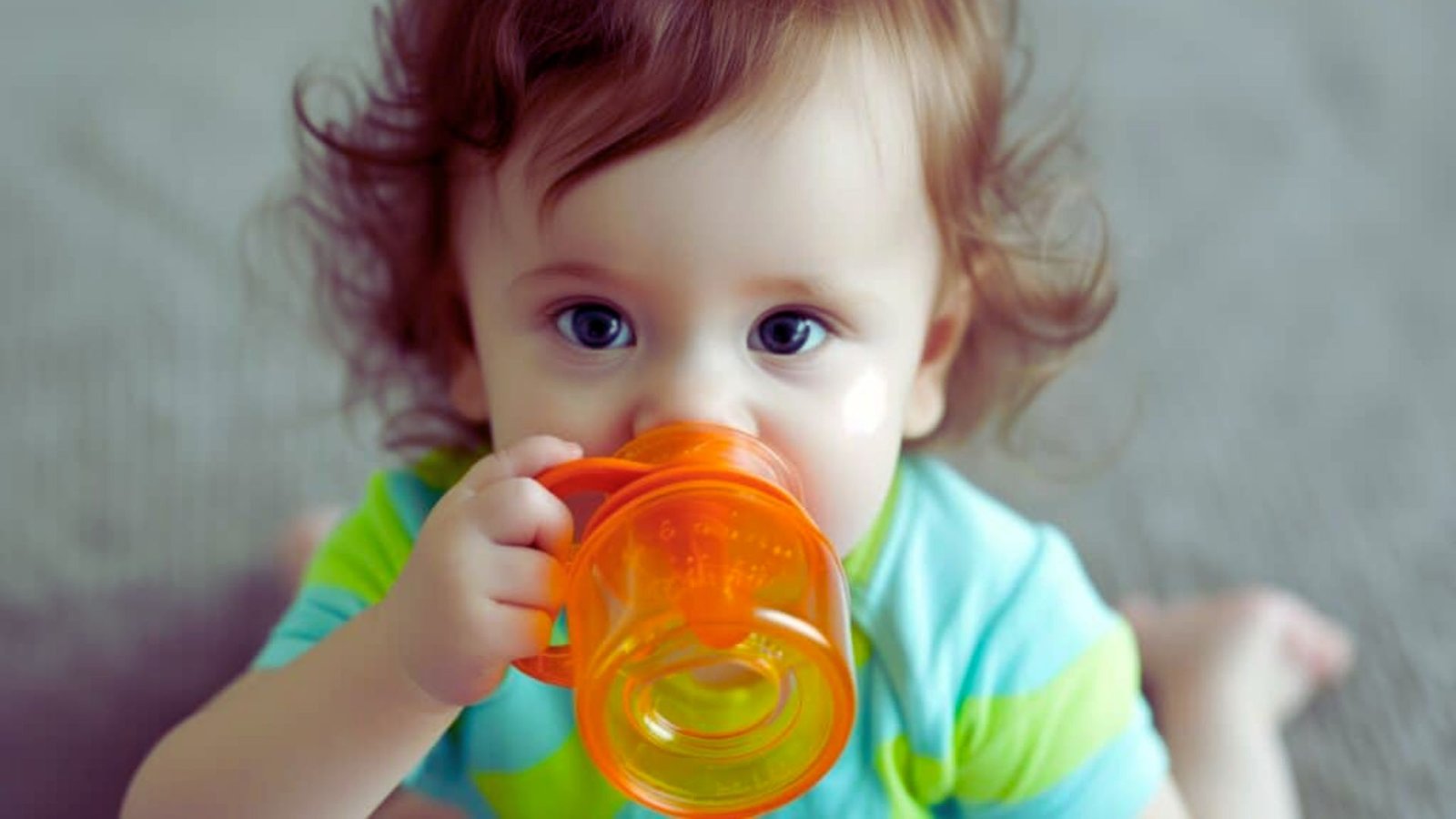 A baby happily drinking from a bottle, with a focused expression and small hands holding the bottle securely