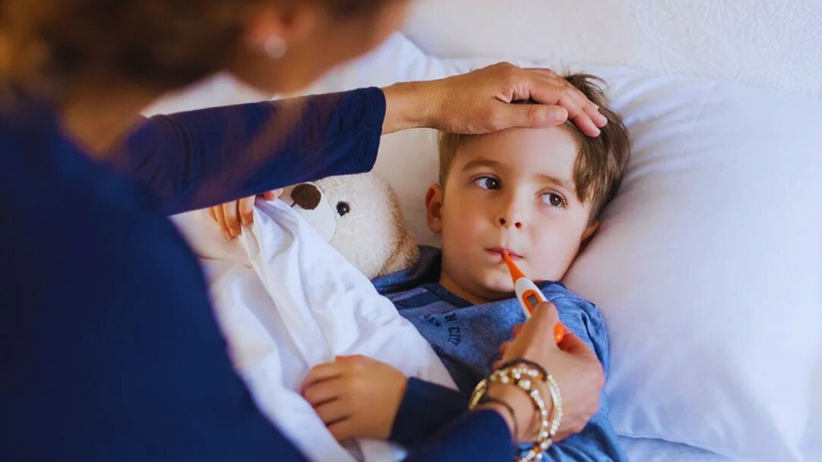 A woman gently holds a child's hand while he rests in bed, creating a comforting and nurturing atmosphere.