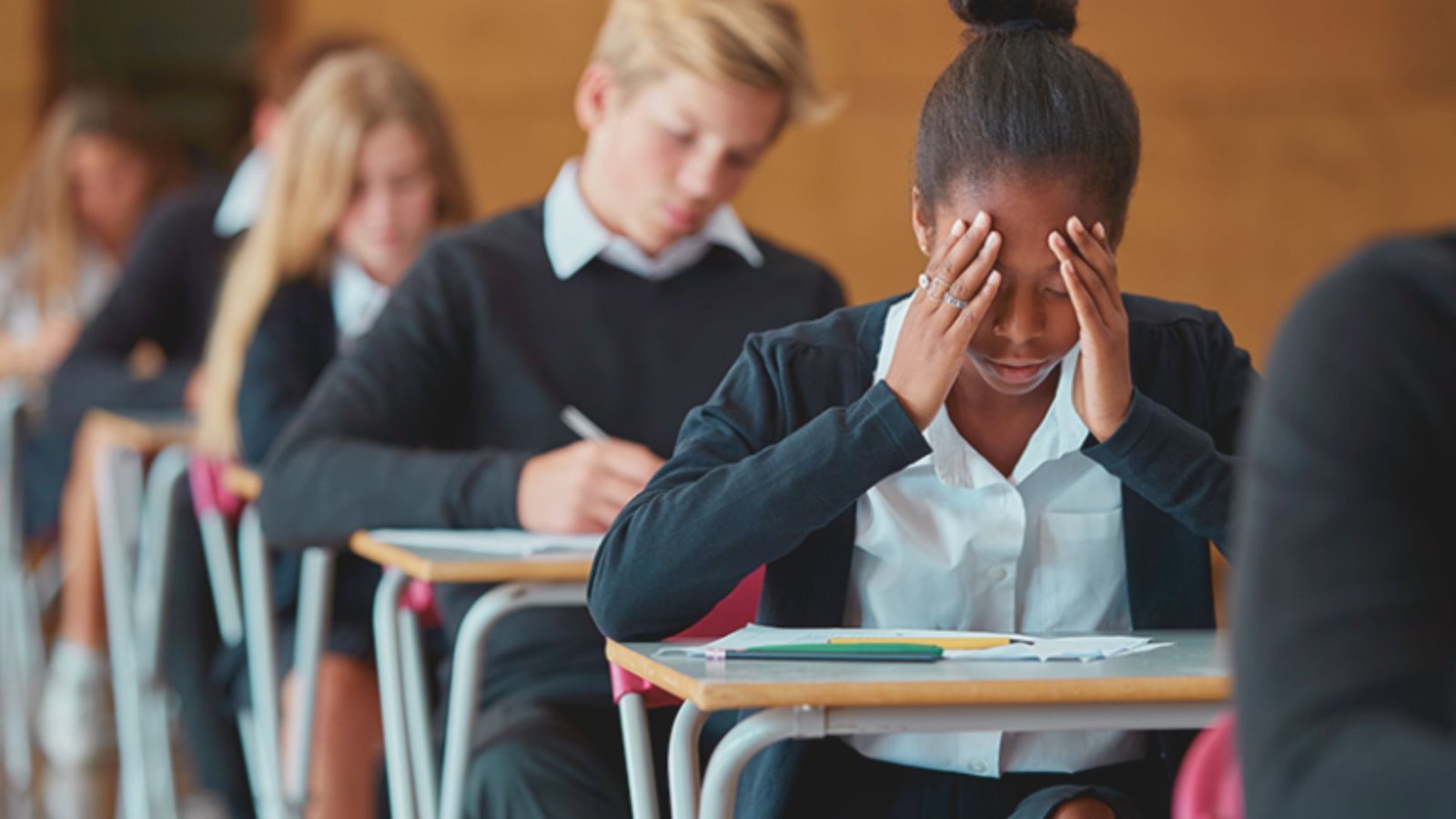 A girl with her head in her hands at a desk, suggesting feelings of anxiety or contemplation.