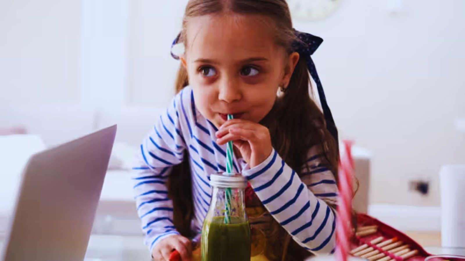 A young girl happily sipping a green smoothie from a glass, showcasing her enjoyment of a healthy drink.