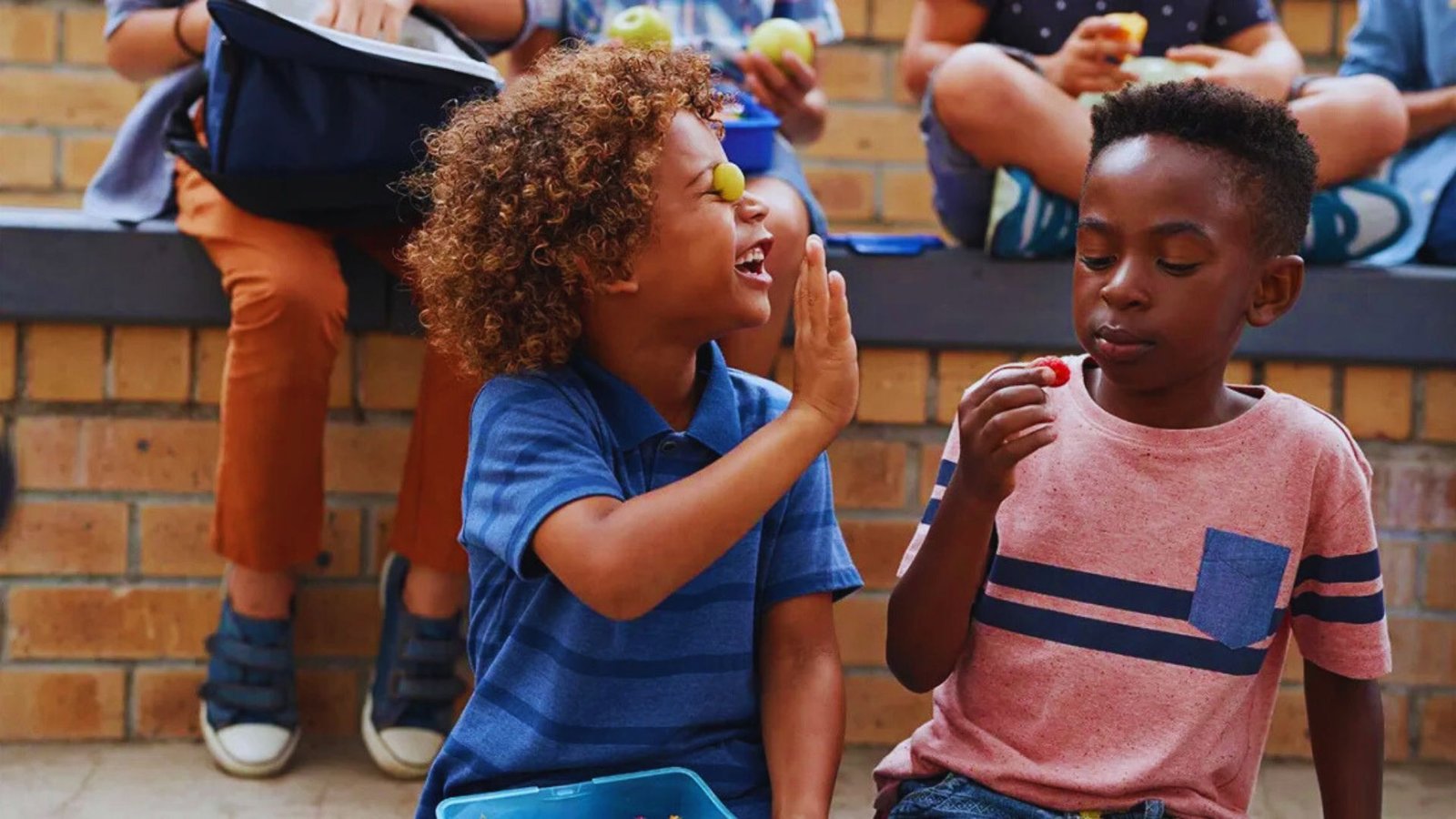 Two children sitting on the ground, happily eating apples together.
