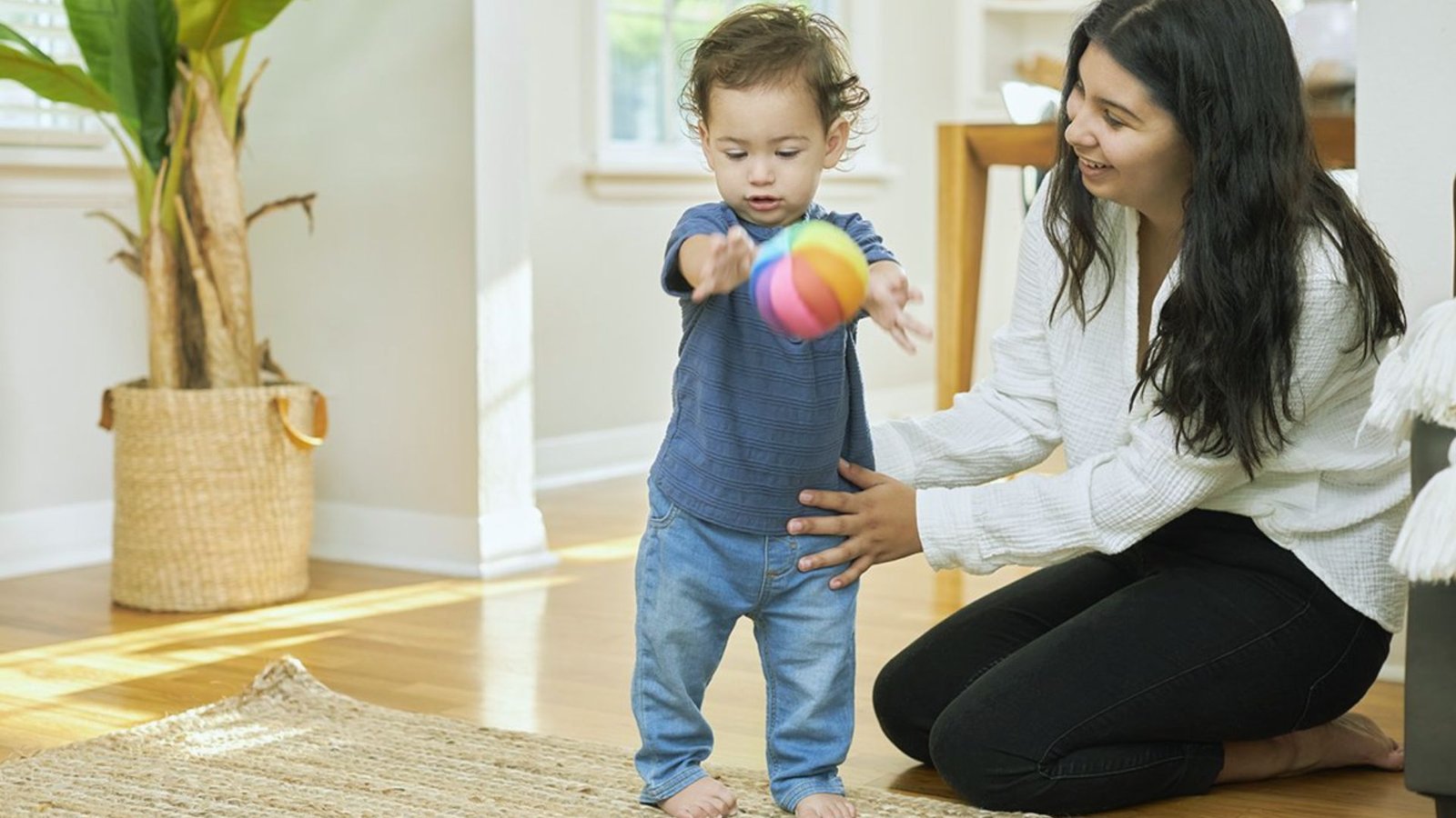 A woman and a child joyfully playing together with a colorful ball in a sunny Indoor setting.
