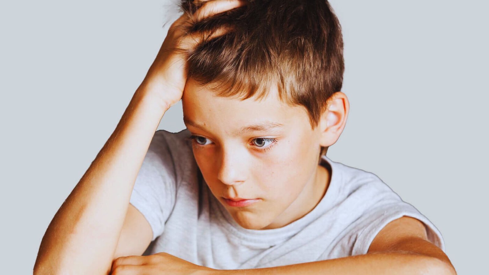A boy sits with his head resting on his hand, appearing thoughtful or contemplative.