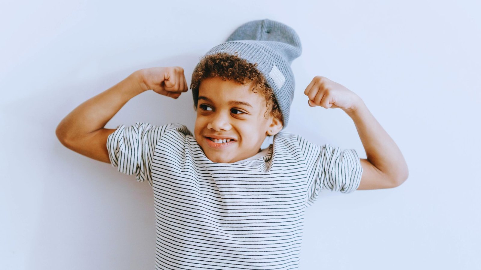 A young boy proudly flexes his muscles, showcasing his strength and confidence with a big smile on his face.