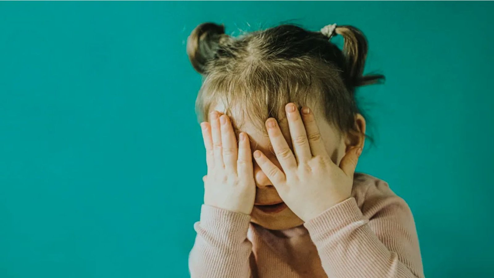 A little girl covering her eyes with her hands, expressing surprise or anticipation.