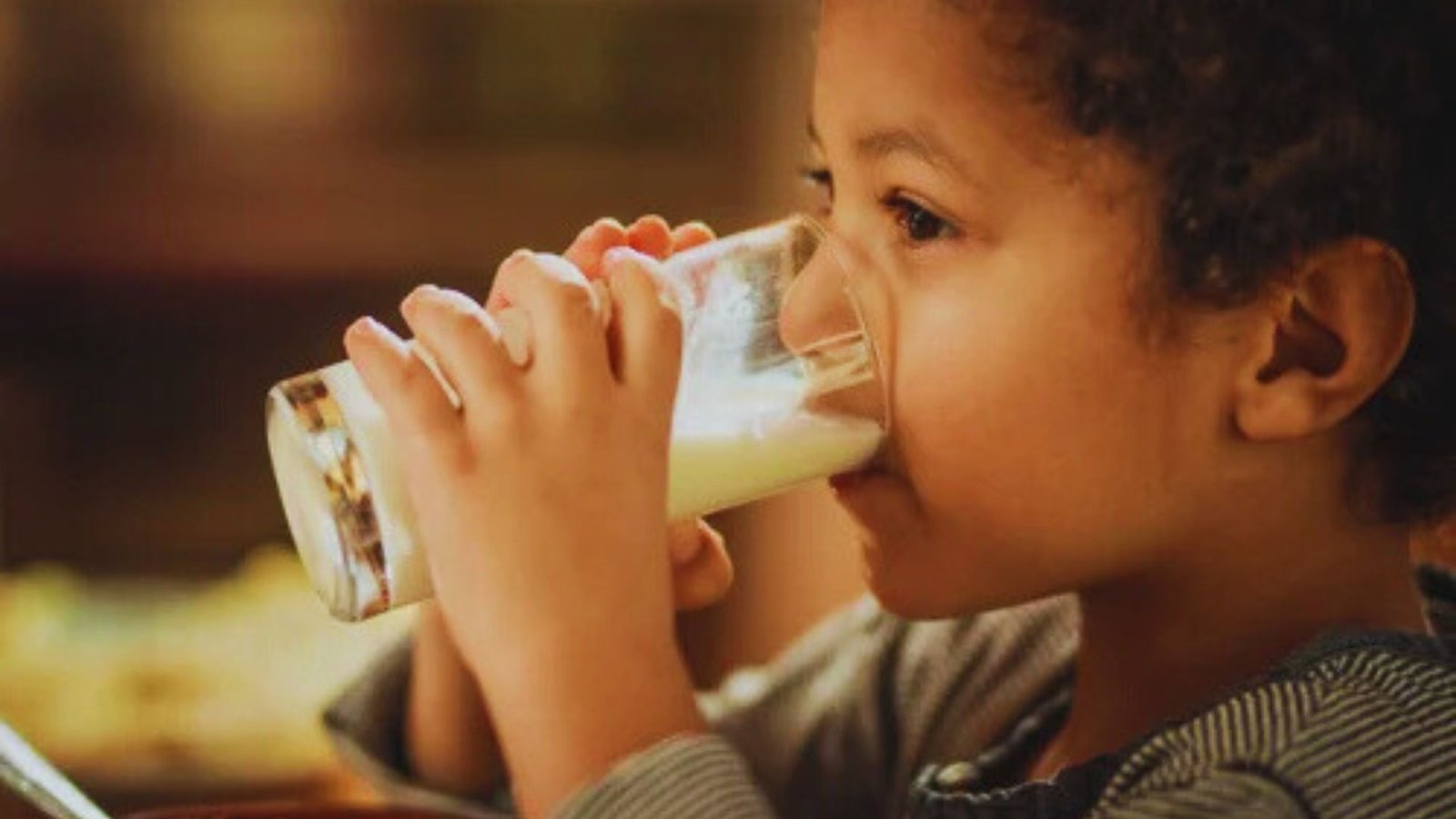 A young child happily drinking milk from a clear glass, with a joyful expression on their face.