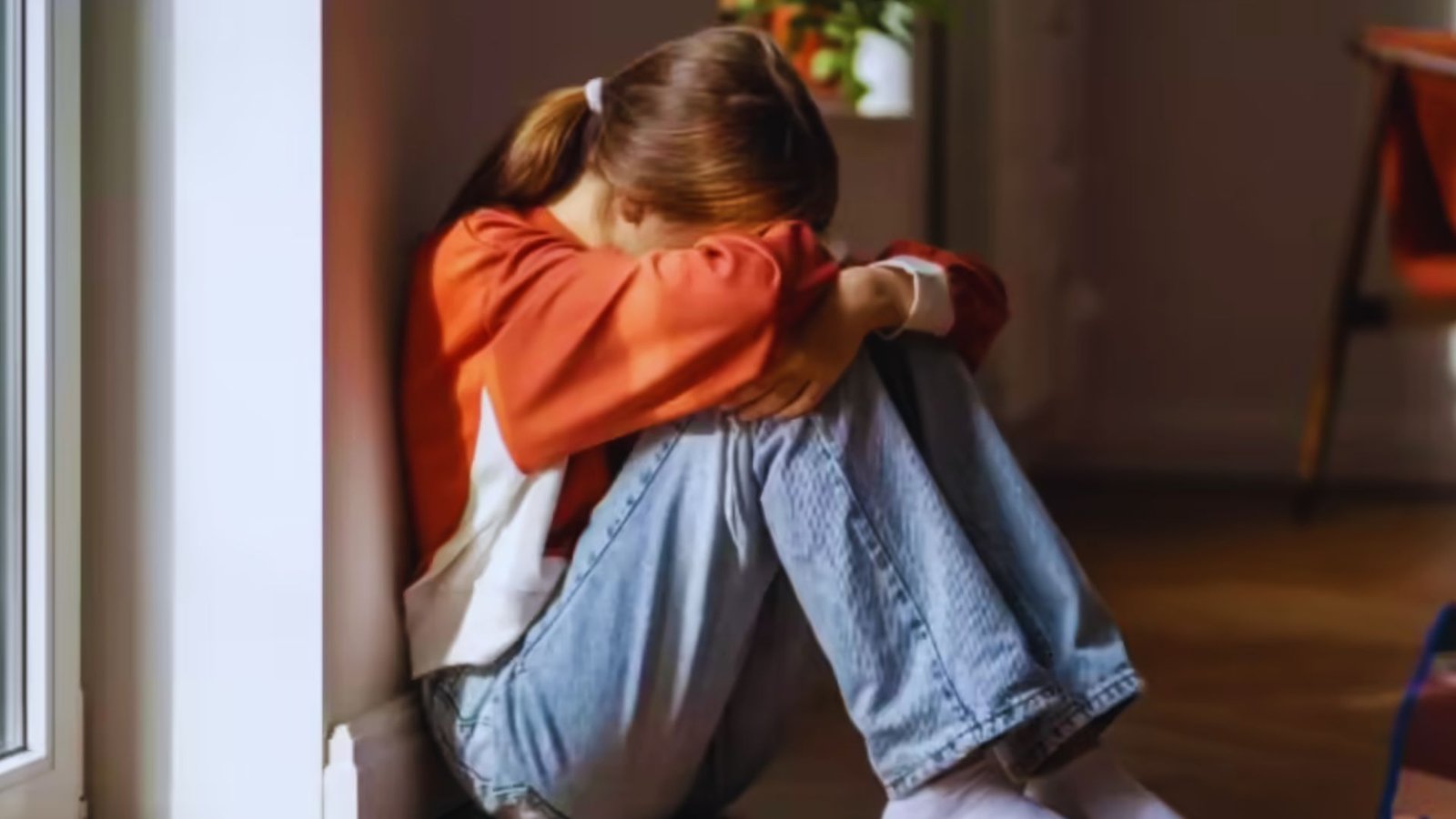 A young girl sitting on the floor, resting her head in her hands, conveying a sense of sadness or distress.