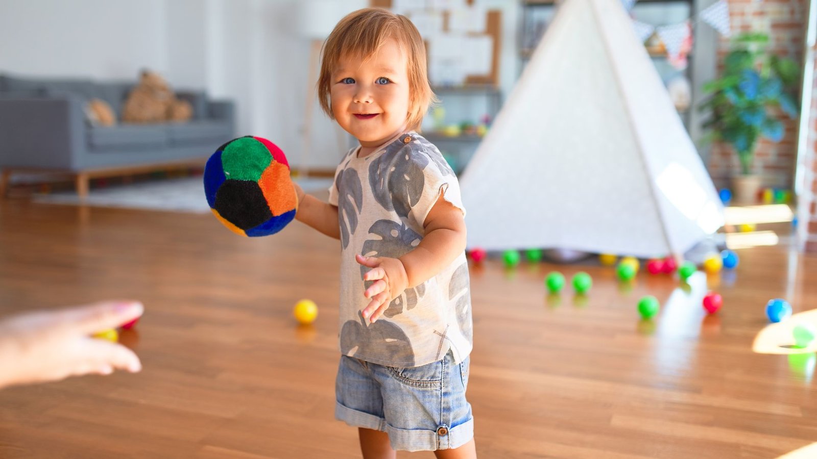 A child joyfully playing with a colorful ball in a bright, spacious room.