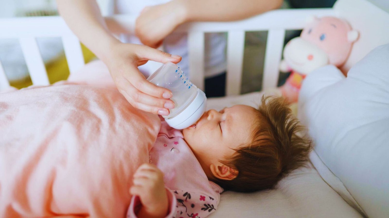 A baby in a crib is being fed with a bottle, looking content and relaxed during mealtime.