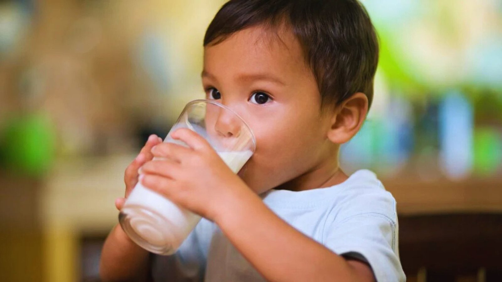 A young boy happily drinks milk from a glass, enjoying a refreshing moment.
