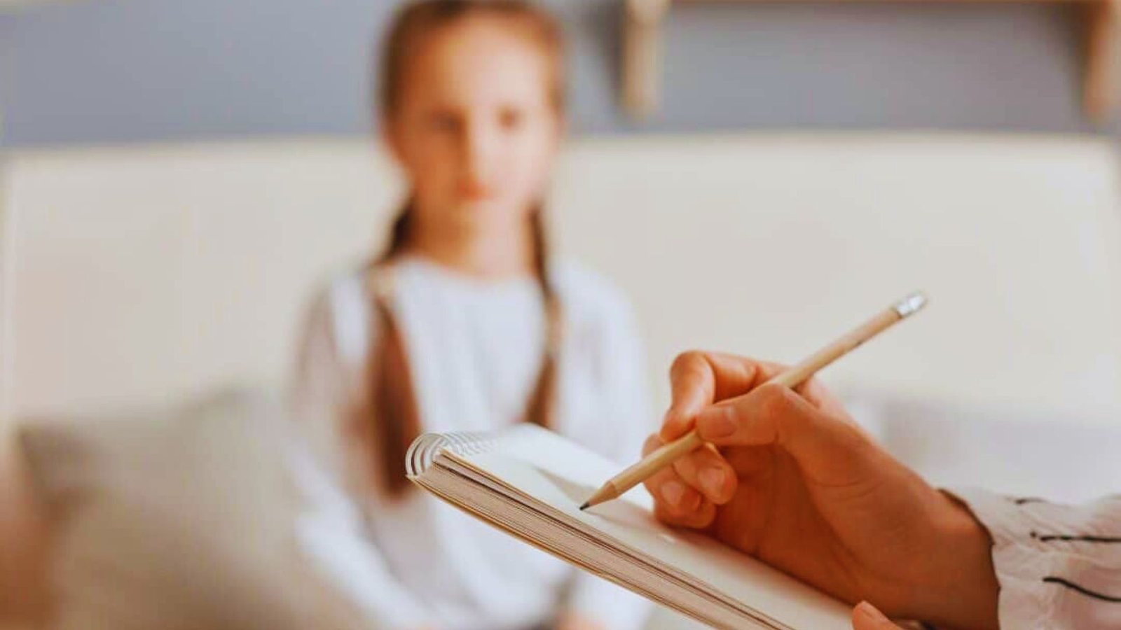 A child sits in front of a white background, focused on writing with a pen on paper.
