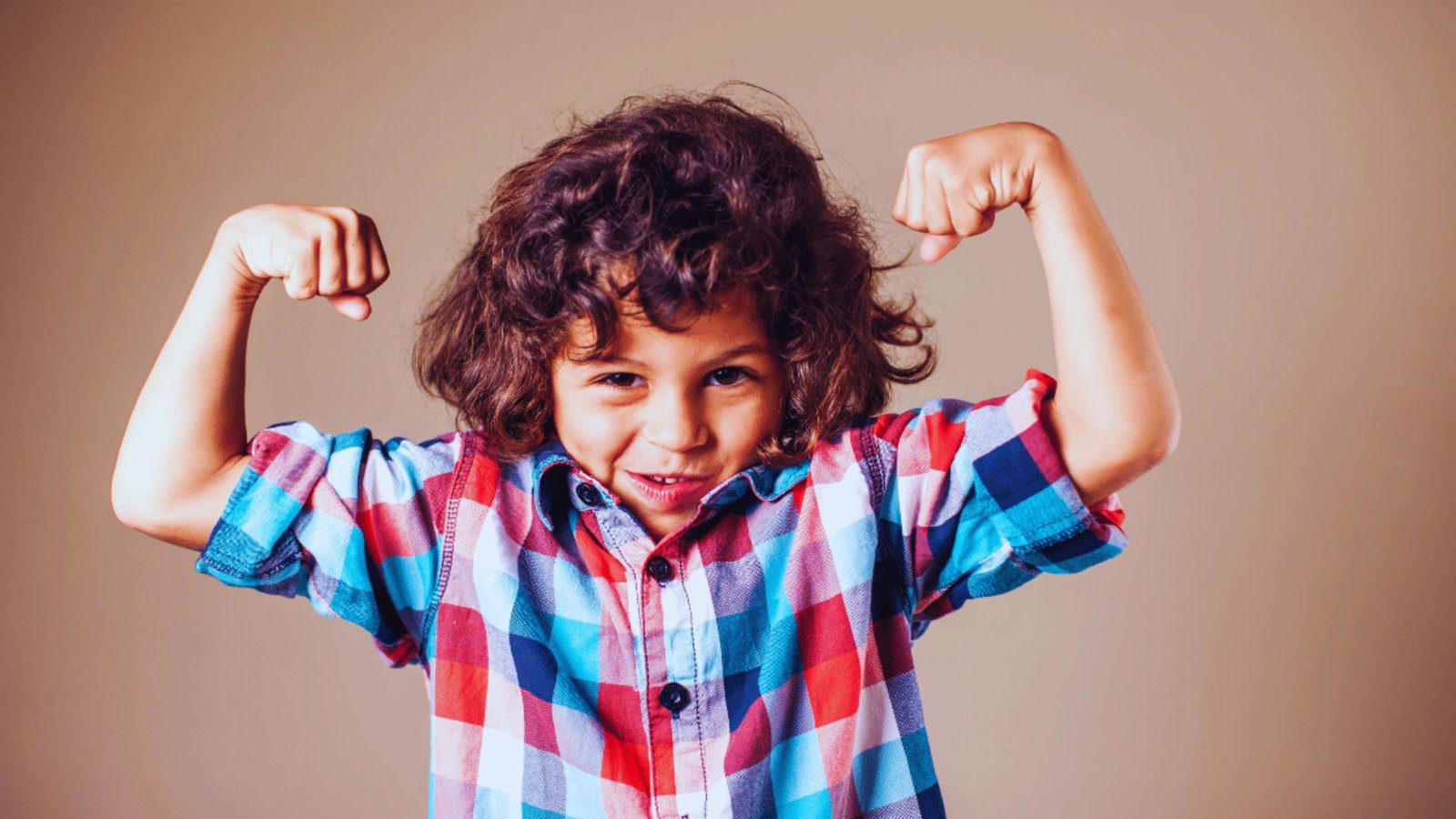 A young boy proudly flexing his muscles, showcasing his strength and confidence with a big smile on his face.