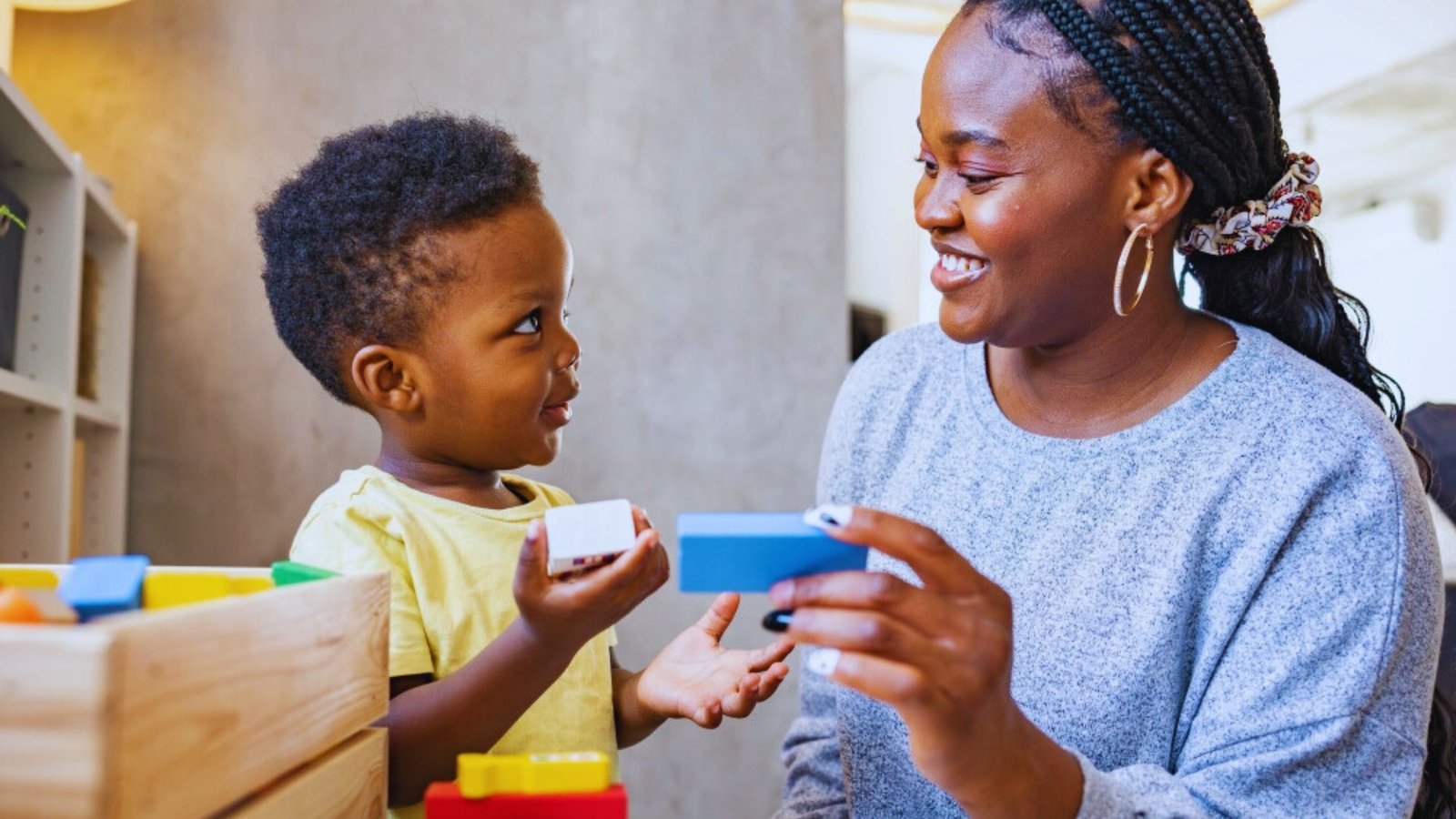 A woman and a child joyfully playing together with colorful toys on a soft carpet.