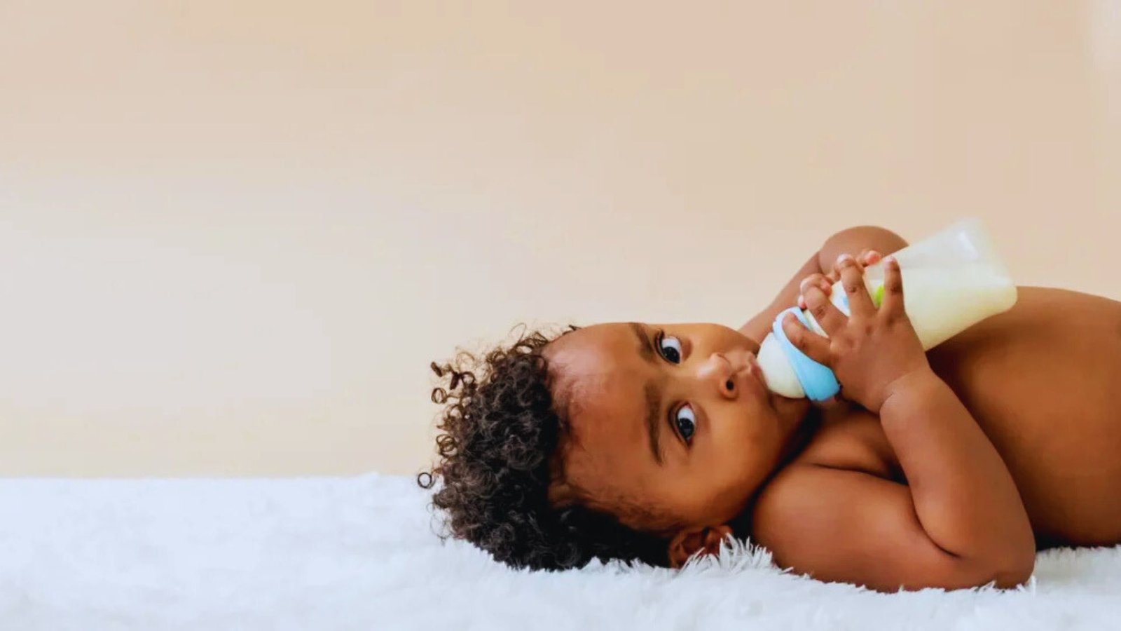 A baby lying on a white blanket, holding a bottle, with a peaceful expression on their face.