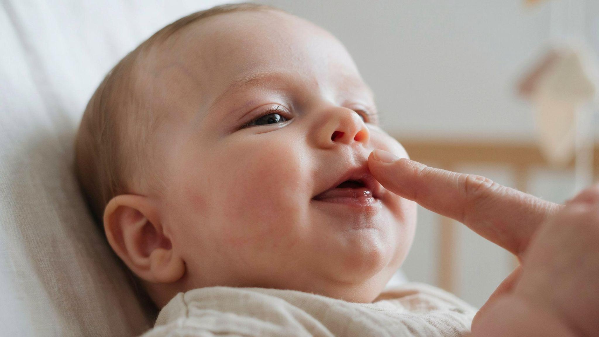 Baby smiling with healthy pink gums before teeth erupt, gentle gum massage, soft natural nursery lighting.