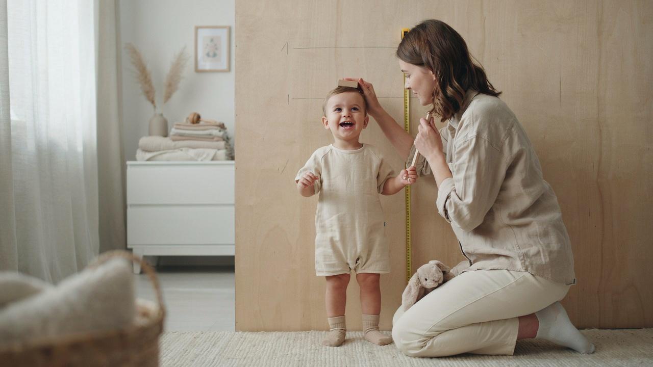 Parent measuring baby's height to determine if size 80 baby clothes will fit.
