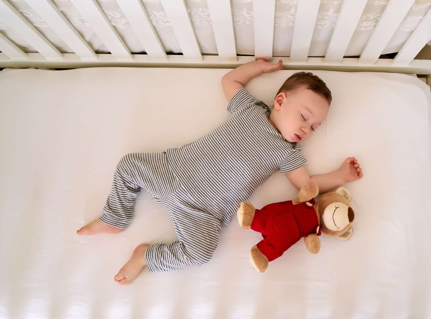 Sleepy baby with pacifier rhythmically rocks head on crib mattress to self-settle before falling asleep