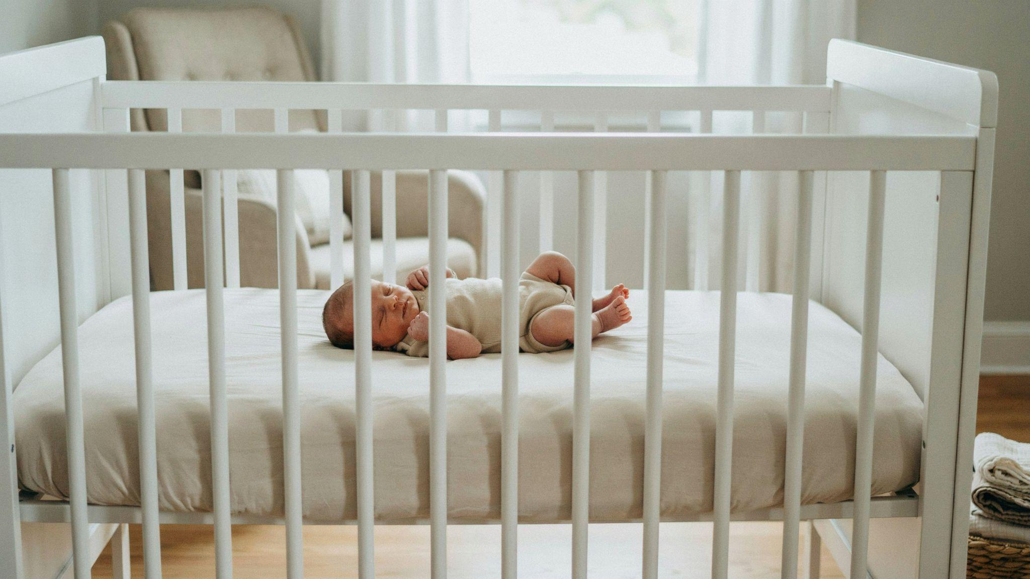 Newborn baby sleeping safely on back without swaddle in a simple safe sleep crib