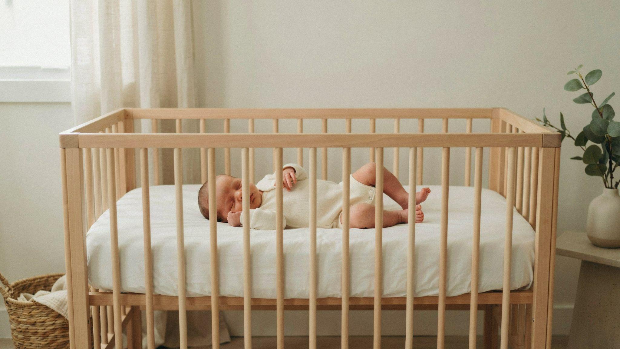 Newborn baby sleeping safely on back in crib without swaddle wearing a comfortable sleep onesie