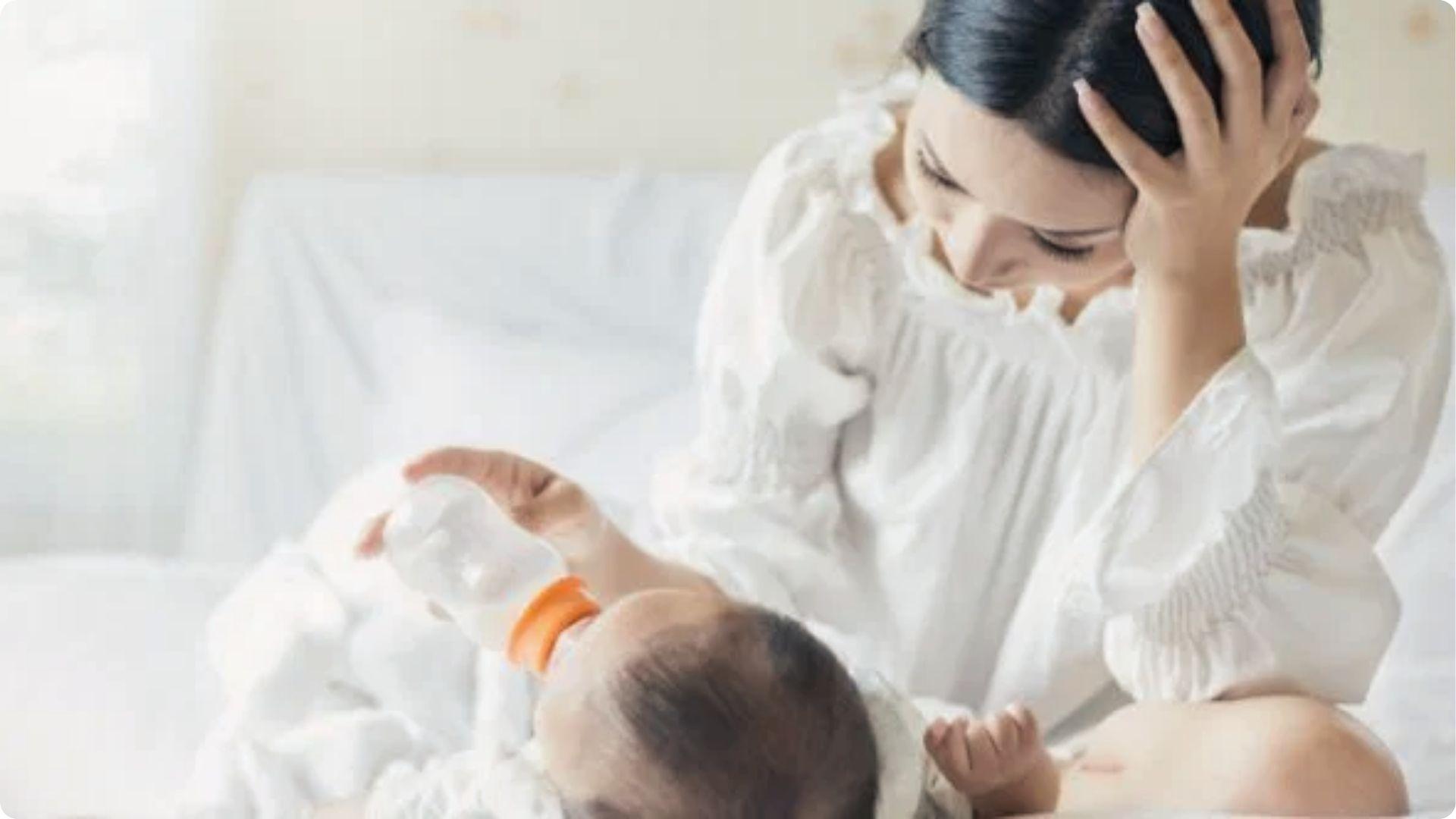 Worried mom bottle-feeding baby on bed; head shaking can signal hunger, discomfort, or self-soothing.
