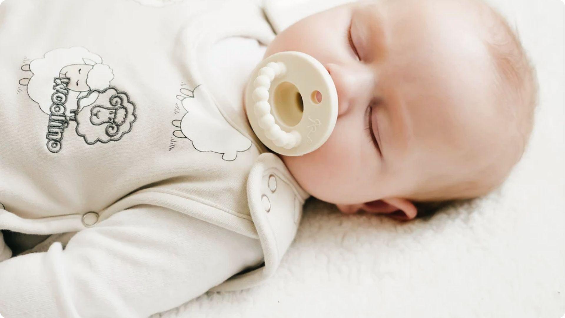 Sleeping baby in sheep onesie with white pacifier, showing pacifiers may aid infant sleep routines.