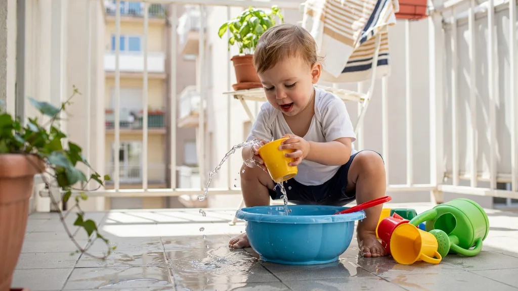 Toddler enjoying safe water play with cups and containers.