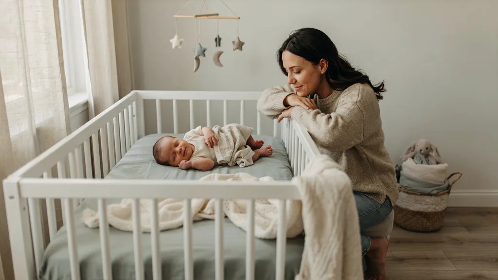 Baby smiling peacefully while sleeping in a cozy nursery with a parent nearby.