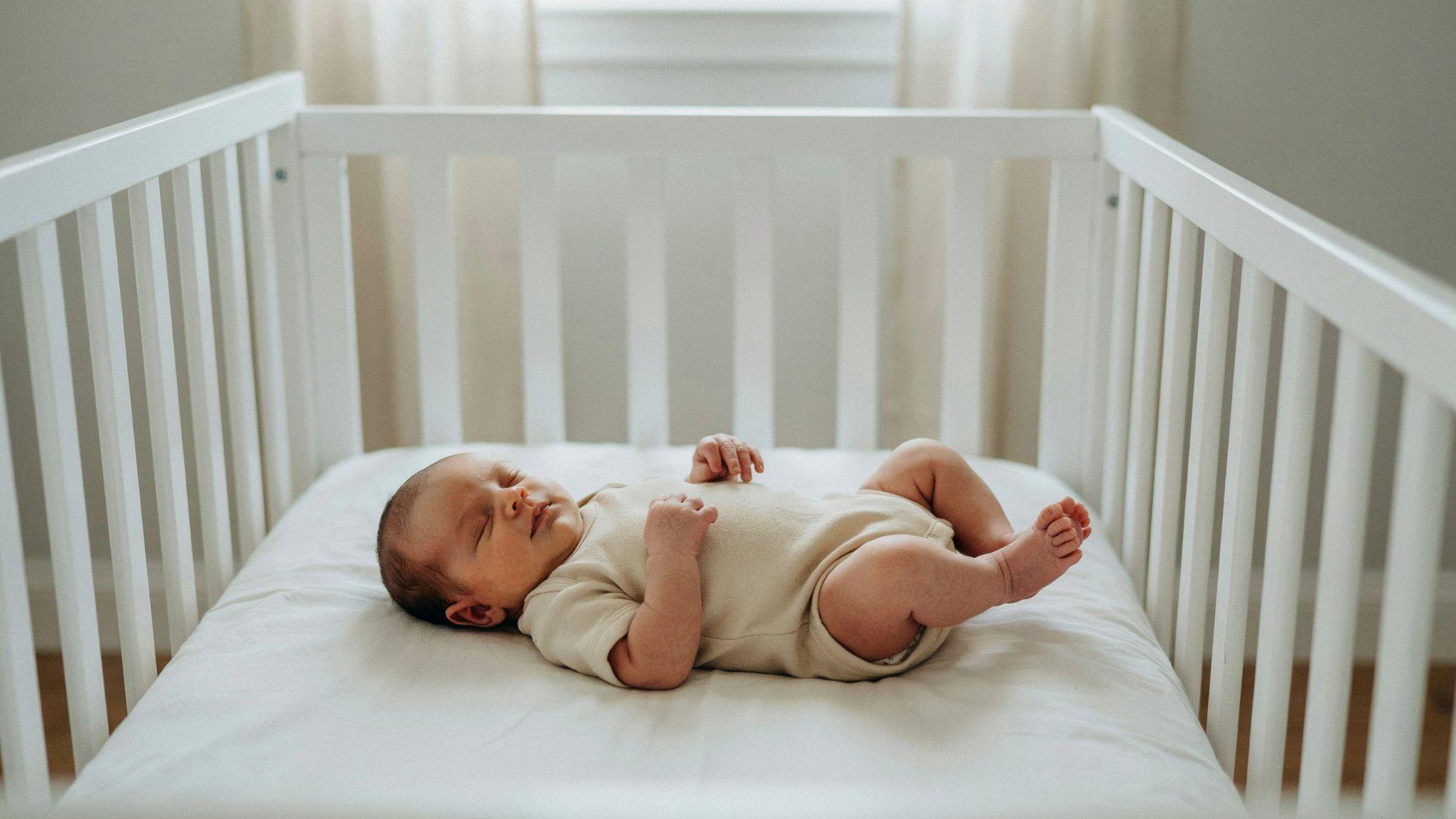 Peaceful newborn sleeping comfortably without a swaddle with arms free in a safe crib