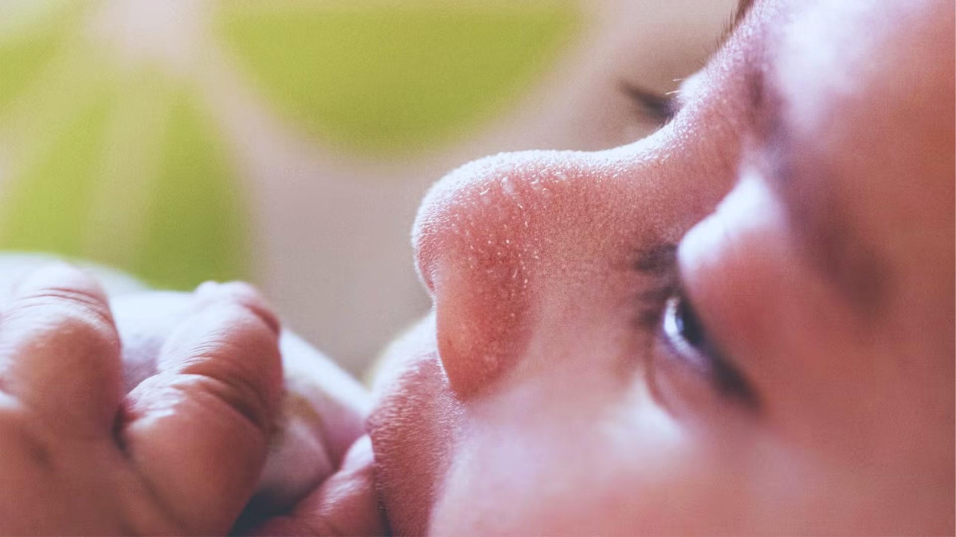 Side profile of baby’s face with sweat droplets on nose, held gently by adult hand.