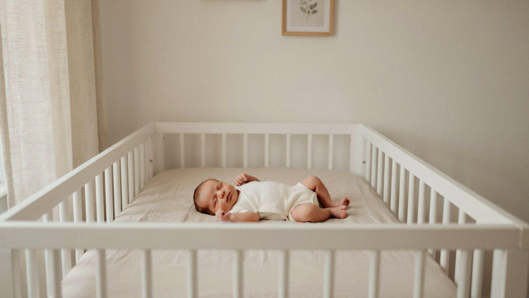 Newborn sleeping safely on back in a clear crib with a firm mattress and fitted sheet