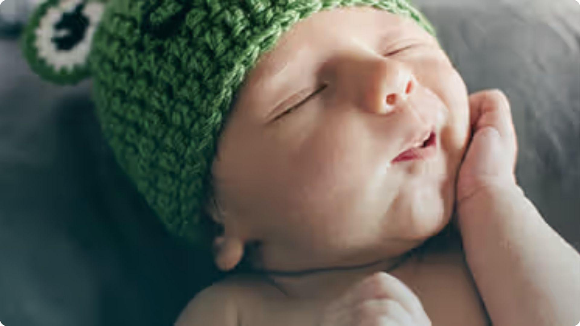 Newborn in green knit hat sleeping peacefully; rhythmic head shaking helps babies self-soothe to sleep.