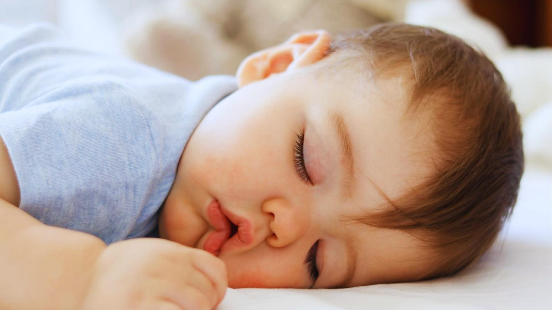 Toddler with light brown hair sleeps on side in blue shirt, mouth open on white pillow.