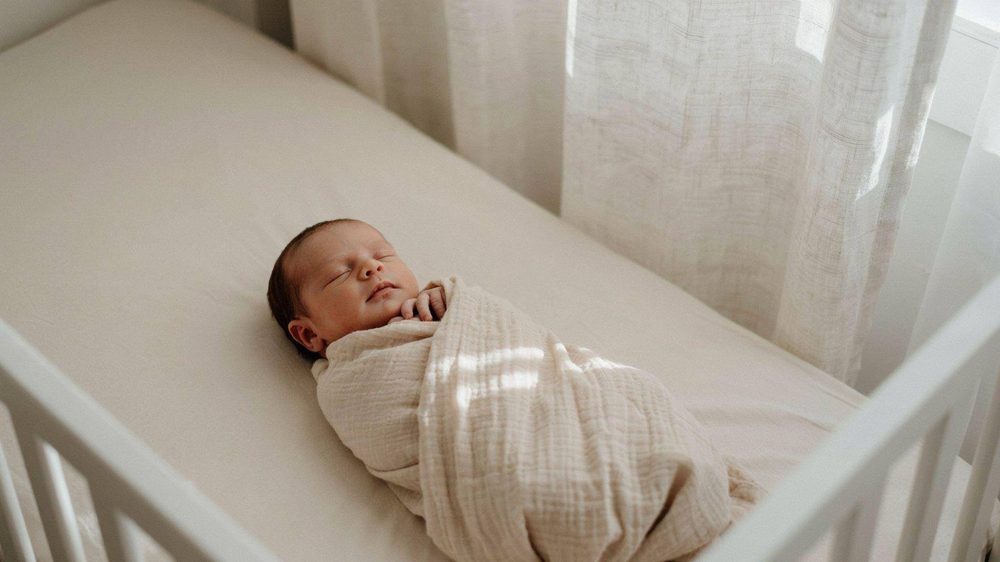Peacefully swaddled newborn resting comfortably in a safe crib with soft breathable blanket