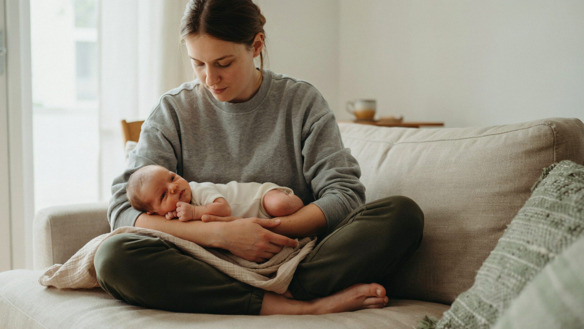 Newborn calmly resting in tummy hold position across parent’s arm.