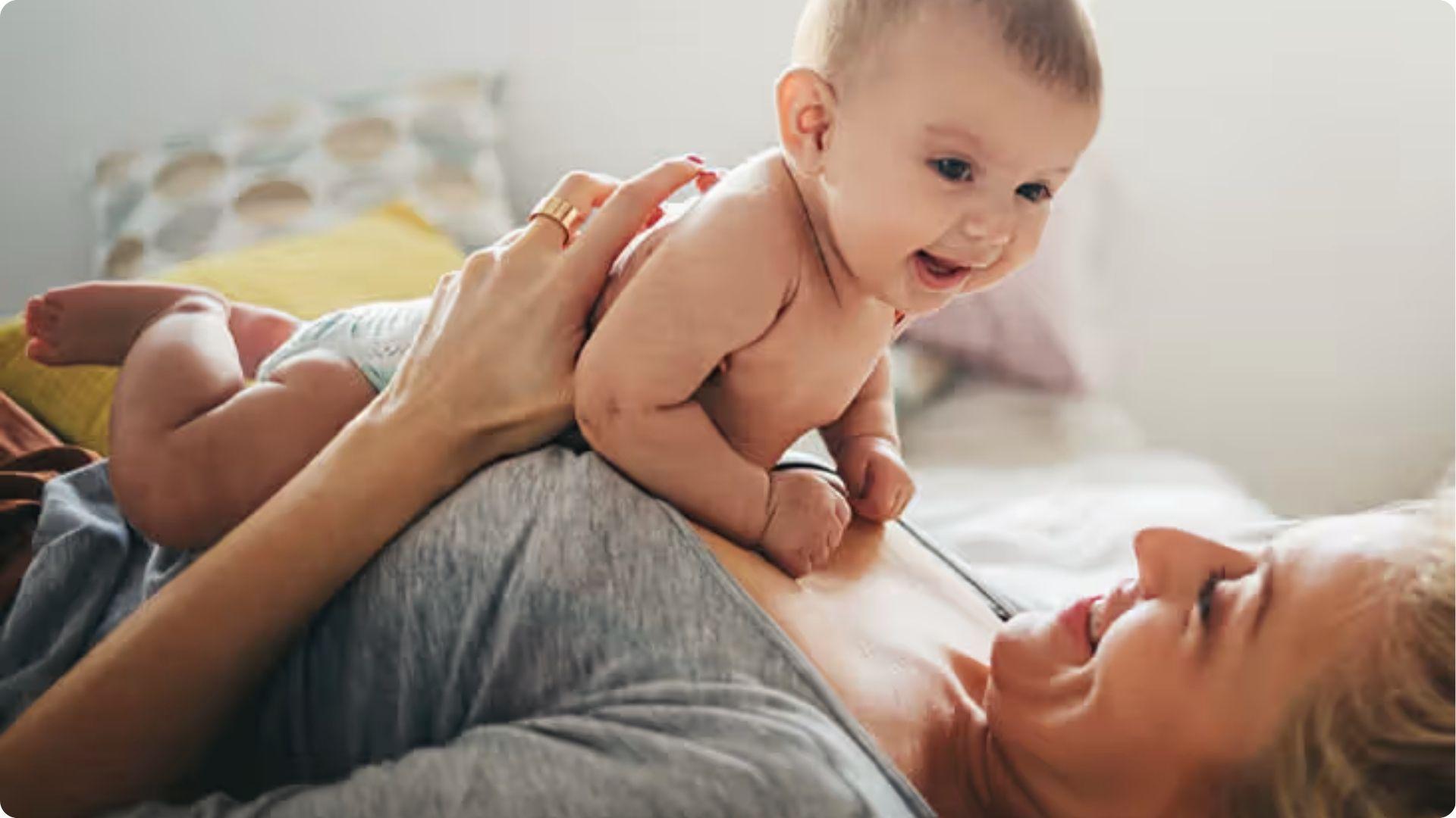 Mom playing with a smiling baby on tummy; head shaking during play can be excitement or practicing moves.
