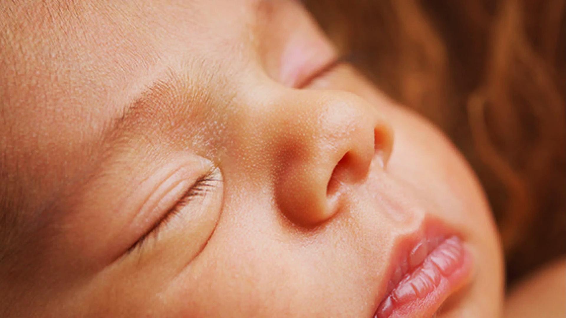 Extreme close-up of sleeping baby’s face showing closed eye, nose, and slightly parted lips.