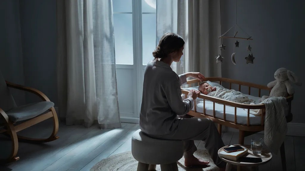Parent watching a sleeping newborn with a pacifier during bedtime.