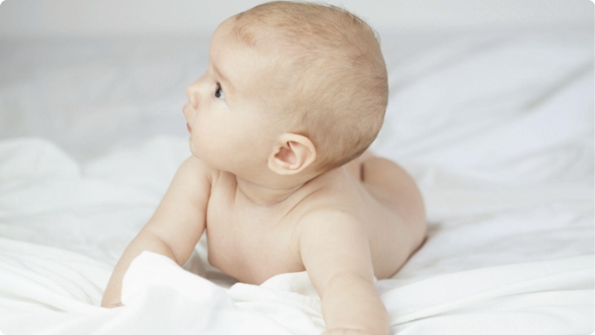 Smiling baby on white blanket shaking head side to side, a common self-soothing reflex before sleep