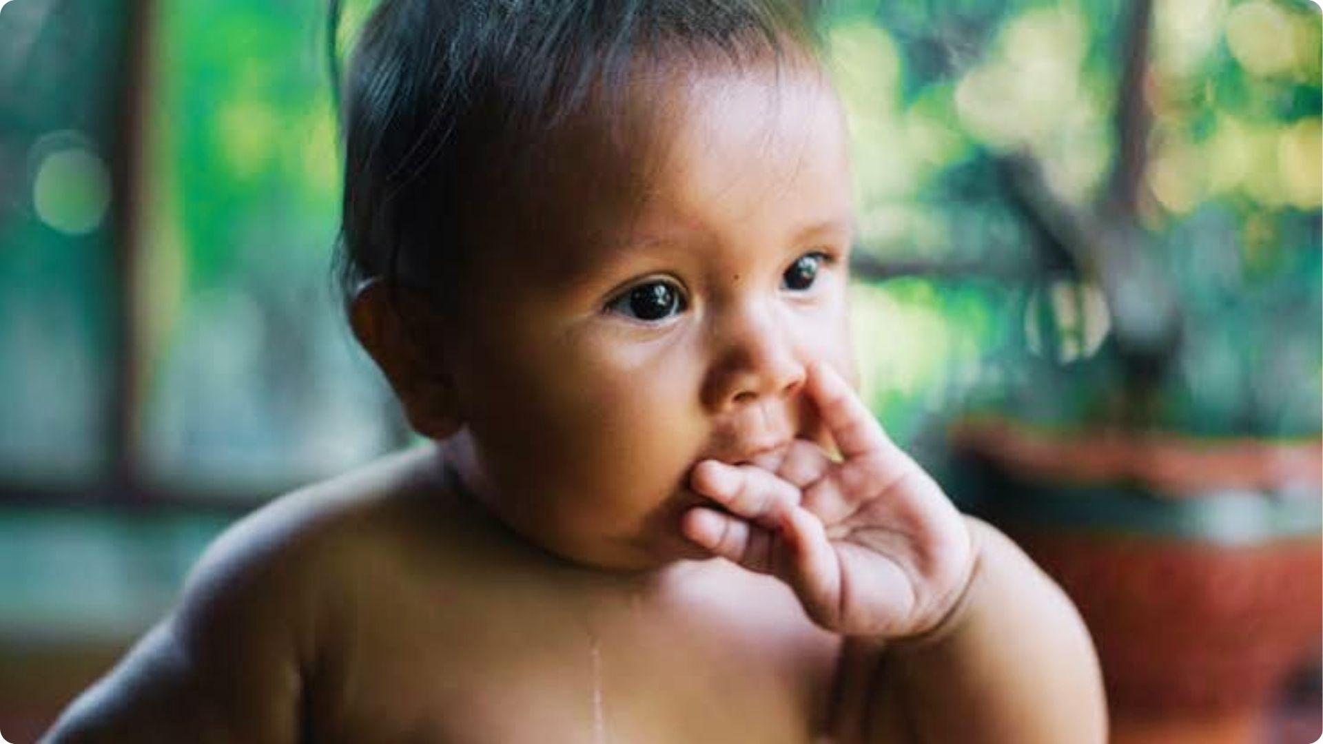 Close-up of infant sucking thumb near window, showing early self-soothing habit starting in womb stage