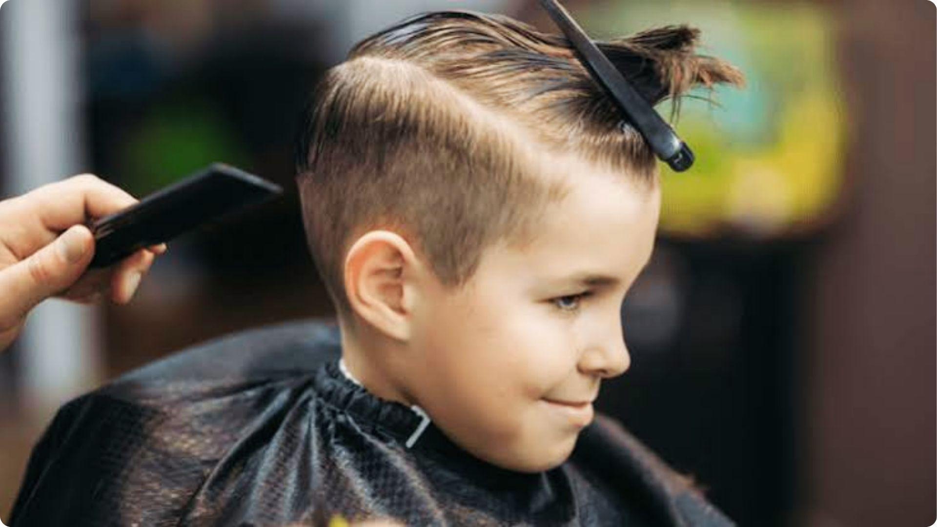 Little boy getting stylish side-part haircut at barber shop with comb lifting top hair, trendy fade.