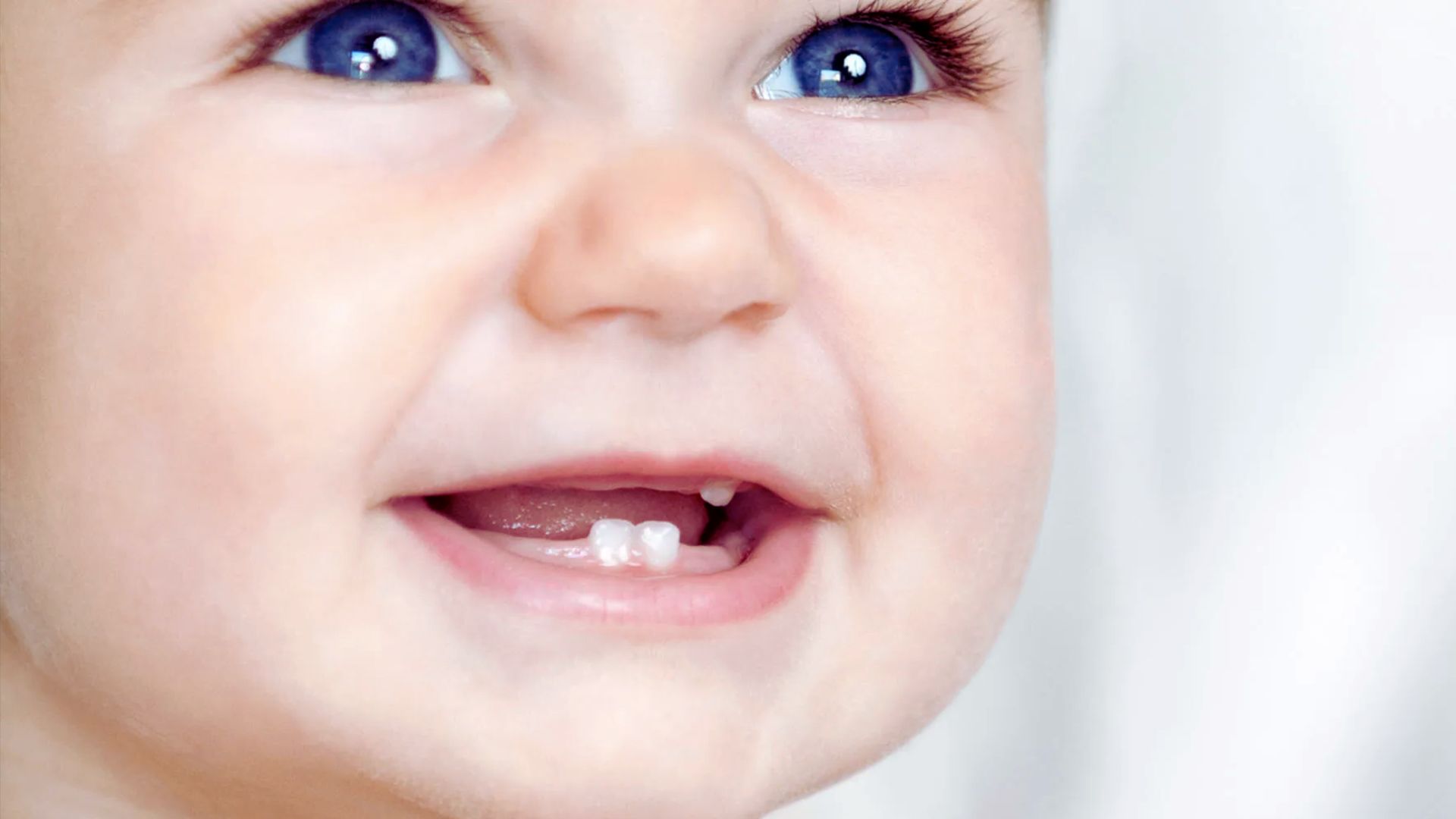 Happy baby smiling showing two lower teeth and one upper tooth, joyful teething milestone