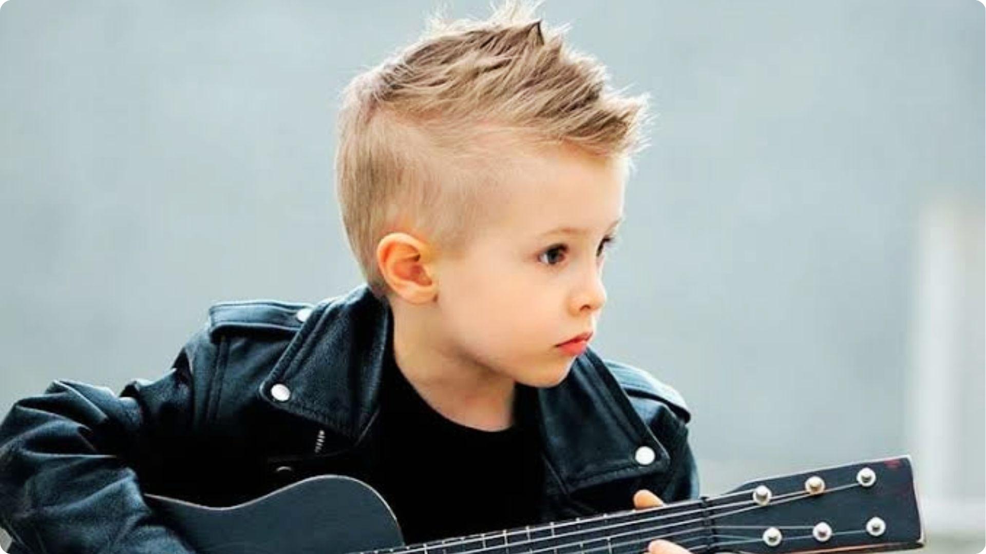 Toddler with spiky faux hawk and high skin fade in leather jacket with guitar, cool modern haircut.