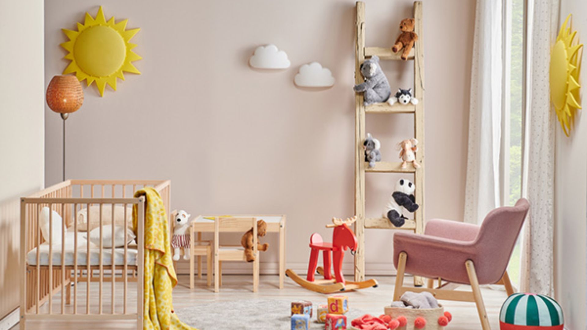 Sunny baby nursery with wooden crib and yellow blanket, pink chair, wooden ladder shelf with stuffed animals, sun and cloud wall decor.