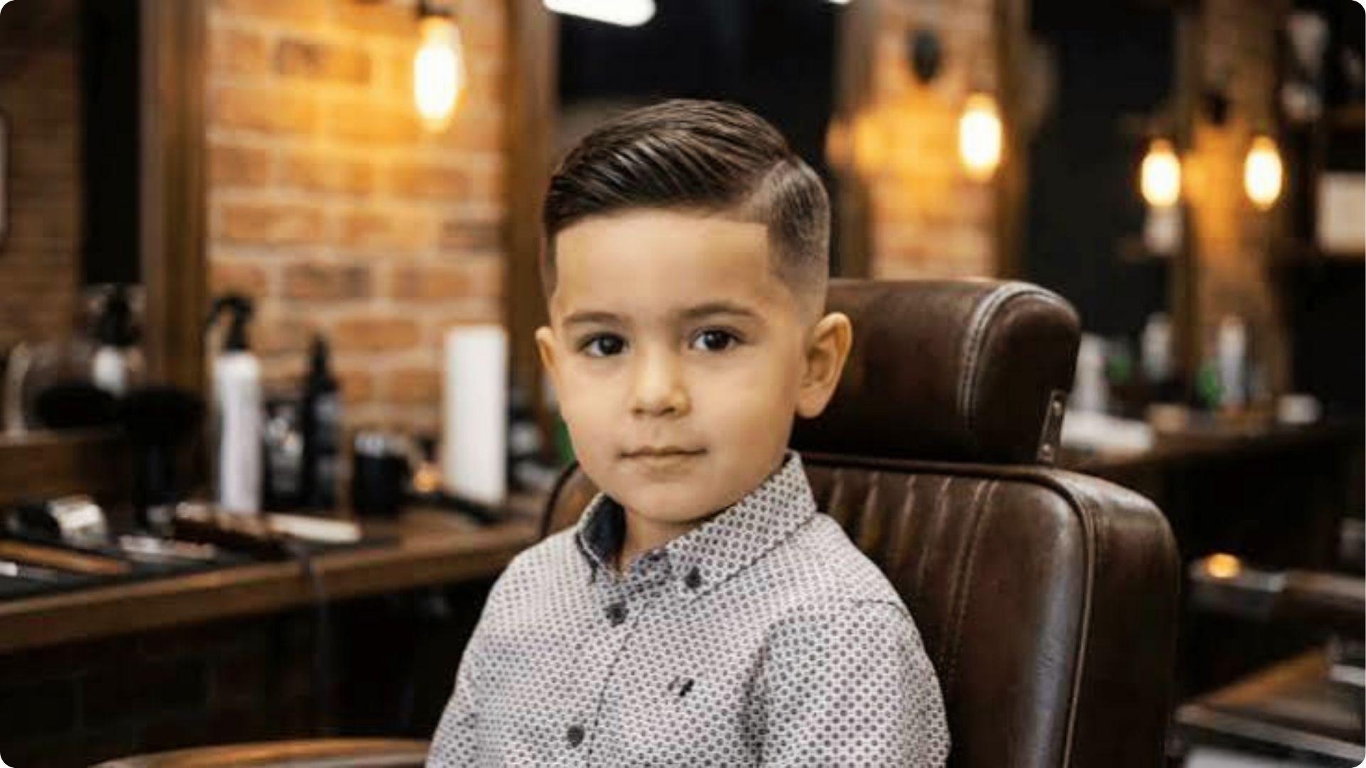 Toddler in barber chair with slick side-combed hair and low fade with line, dapper bab.